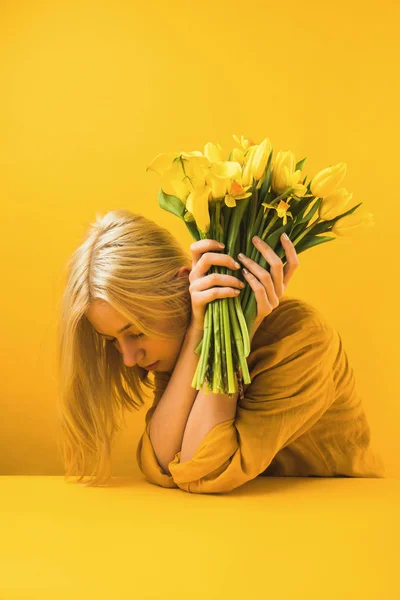 Girl holding beautiful yellow tulips and daffodils on yellow — Stock Photo