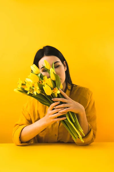 Дівчина тримає красиві жовті весняні квіти на жовтому — стокове фото