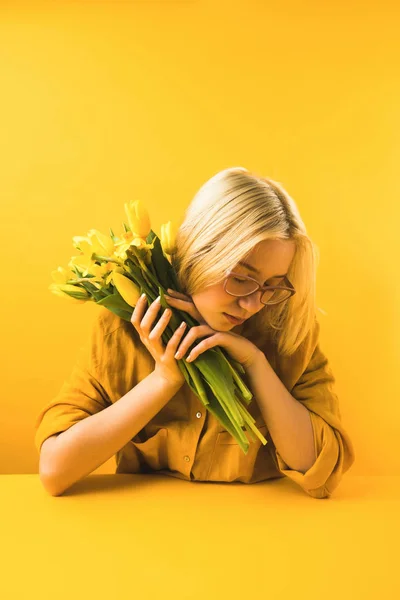 Молода жінка тримає красиві жовті весняні квіти на жовтому — стокове фото