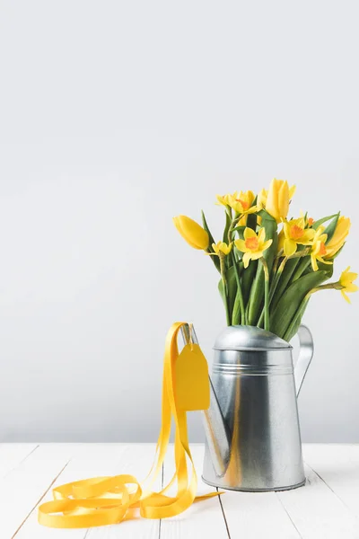 Beautiful yellow spring flowers in watering can on grey — Stock Photo