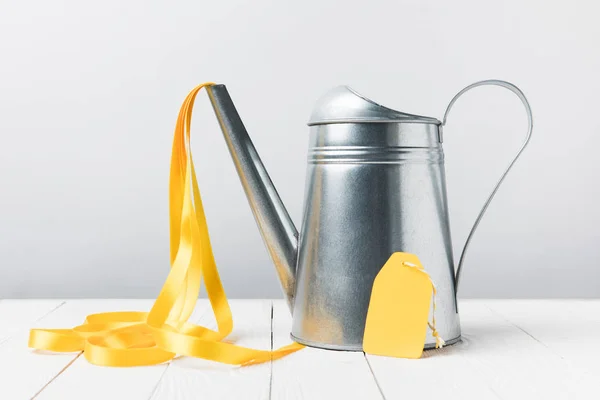 Close-up view of shiny watering can with yellow ribbon and blank label on grey — Stock Photo