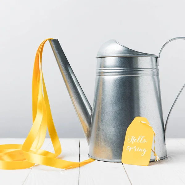 Close-up view of shiny watering can with yellow ribbon and hello april lettering on tag — Stock Photo