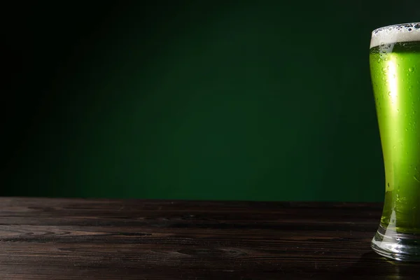 Vaso de cerveza verde con espuma sobre mesa de madera, concepto de día de San Patricio - foto de stock