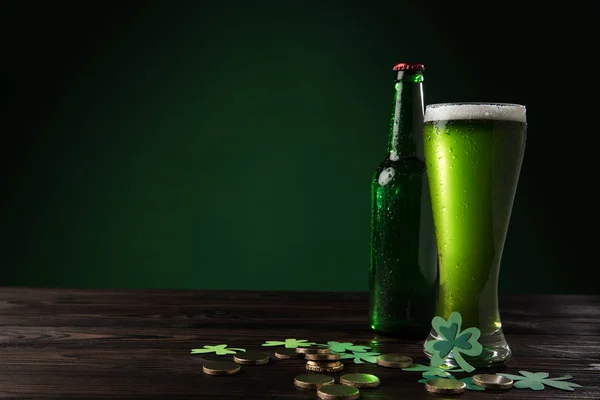 Bouteille en verre et verre de bière verte avec des pièces sur table en bois, st patricks concept de jour — Photo de stock