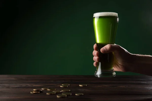 Image recadrée de l'homme tenant verre de bière verte au-dessus de la table avec des pièces, st patricks concept de jour — Photo de stock
