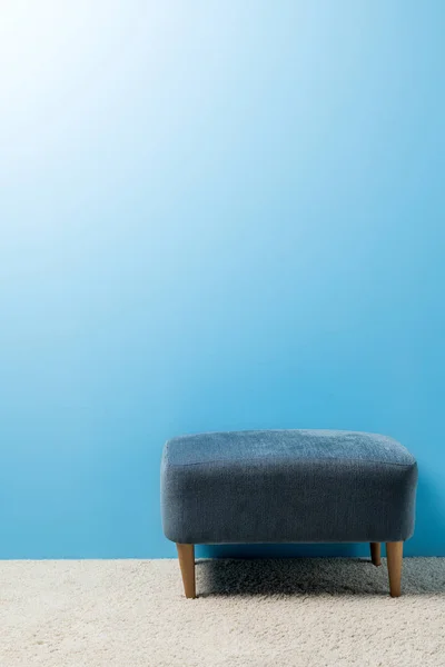 Hassock macio em pé no tapete na frente da parede azul — Fotografia de Stock