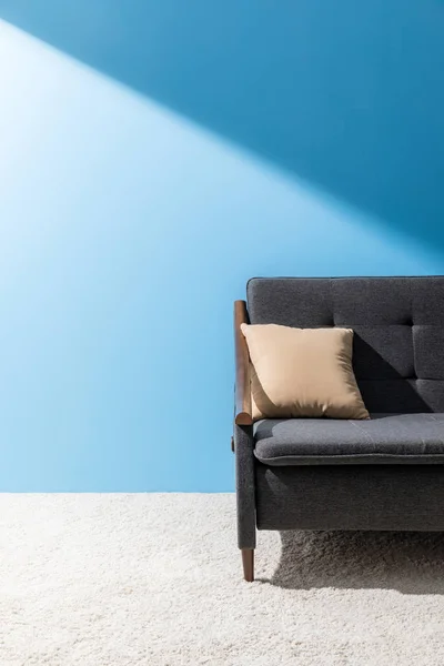 Oreiller couché sur un canapé confortable devant un mur bleu — Photo de stock