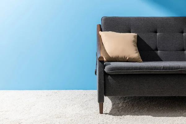 Oreiller couché sur un canapé confortable devant un mur bleu — Photo de stock