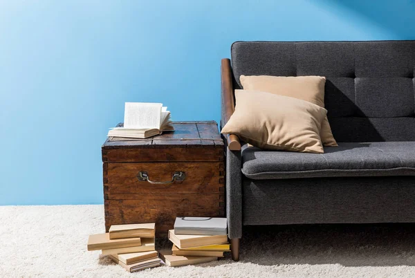 Деревянный сундук с книгами возле дивана перед синей стеной — стоковое фото