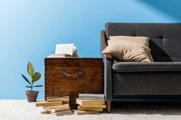 Antigo peito de madeira com livros perto do sofá na frente da parede azul — Fotografia de Stock