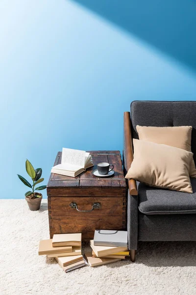 Vieux coffre en bois avec tasse de café et livres près du canapé devant le mur bleu — Photo de stock