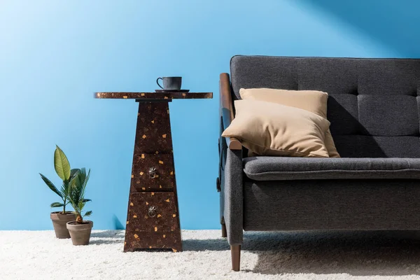 Table basse avec tasse près du canapé devant le mur bleu — Photo de stock
