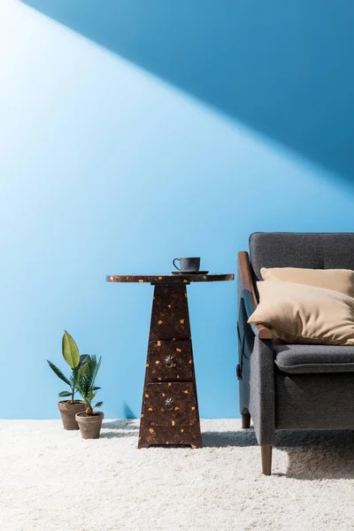Mesa de centro cerca de acogedor sofá en frente de la pared azul — Stock Photo