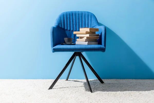 Taza de café y libros en silla delante de la pared azul - foto de stock