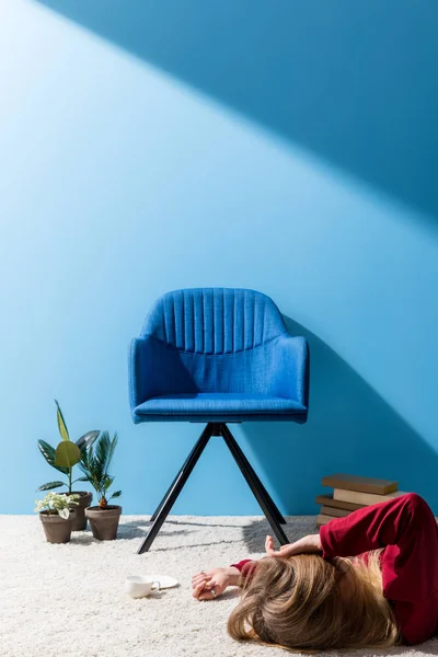 Mujer acostada en el suelo con una taza de café frente a la pared azul - foto de stock