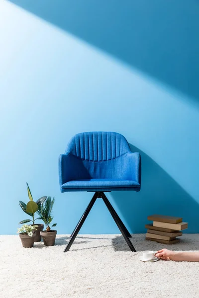 Зручне синє крісло з людиною, що тримає чашку кави на підлозі перед синьою стіною — стокове фото