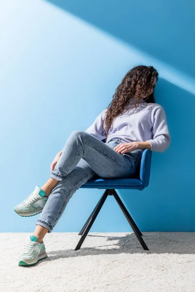 Attraktive junge Frau sitzt im Stuhl vor blauer Wand — Stockfoto