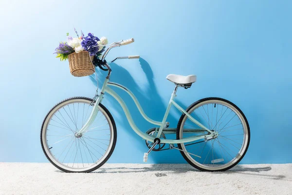 Вид сбоку на велосипед с цветами в корзине перед синей стеной — стоковое фото