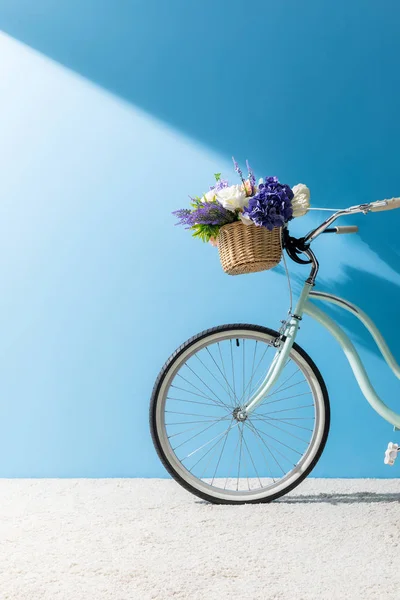 Bicycle with flowers in basket standing on carpet in front of blue wall — Stock Photo