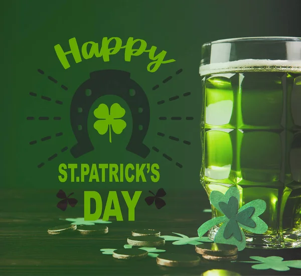 Vista de cerca del vaso de cerveza y monedas en la superficie de madera con letras feliz día de San Patricio - foto de stock