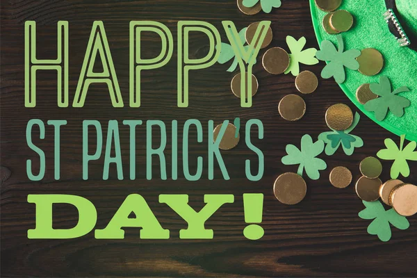 Flat lay with green hat, coins and shamrocks on wooden surface with happy st patricks day lettering — Stock Photo