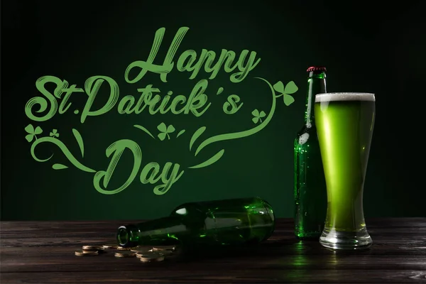 Close up view of glass of beer and bottles on wooden tabletop with happy st patricks day lettering — Stock Photo