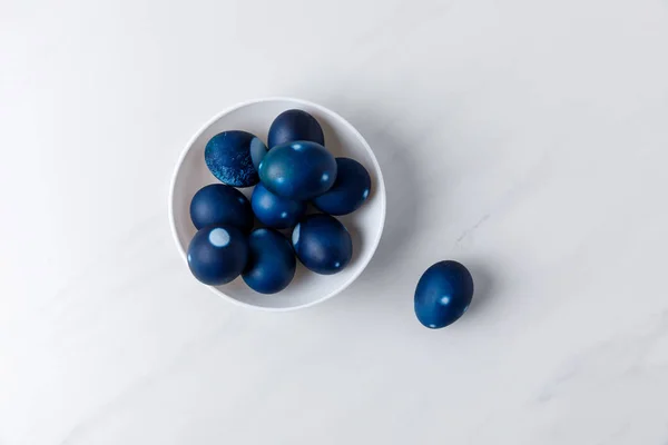 Vista superior de huevos de Pascua pintados de azul en un tazón sobre una superficie blanca - foto de stock