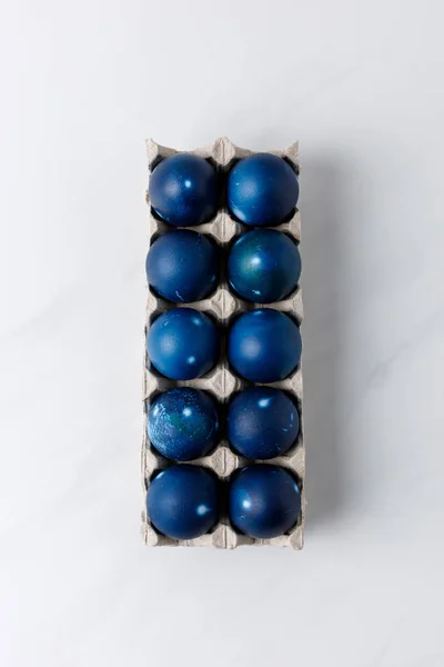Vista dall'alto di uova di Pasqua dipinte di blu in vassoio d'uovo su tavolo bianco — Foto stock