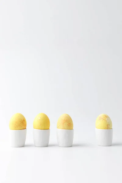 Quattro uova di Pasqua dipinte di giallo in cavalletti di uovo su bianco — Foto stock