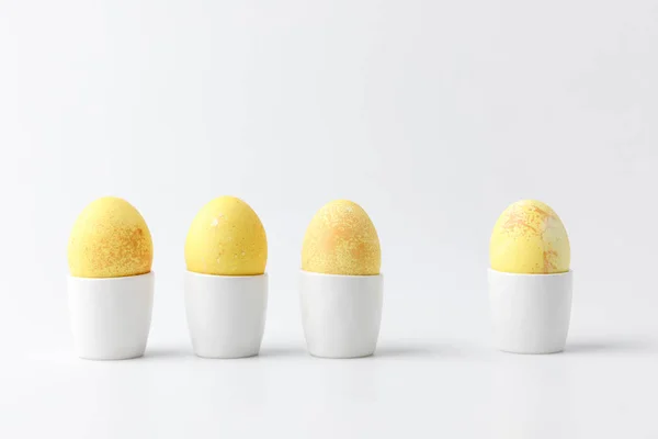 Four yellow painted easter eggs in egg stands on white — Stock Photo