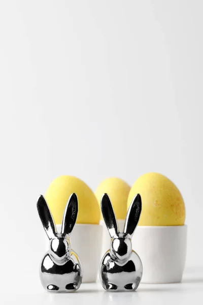 Huevos de Pascua pintados de amarillo en puestos de huevo y estatuillas de conejos sobre blanco - foto de stock