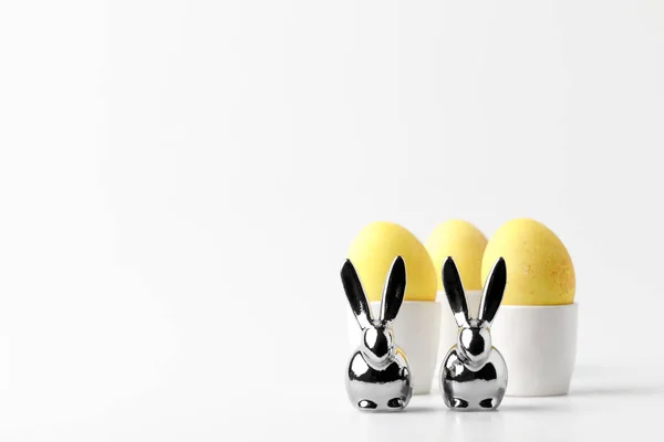 Ovos de páscoa pintados de amarelo em bancadas de ovos e estatuetas de coelhos em branco — Fotografia de Stock