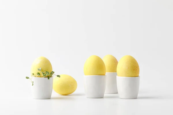 Huevos de Pascua pintados de amarillo en puestos de huevo sobre blanco - foto de stock