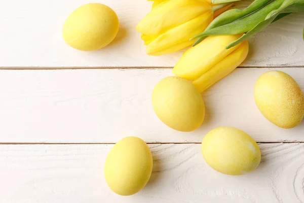 Vista superior de huevos de Pascua pintados de amarillo con tulipanes en la mesa de madera - foto de stock