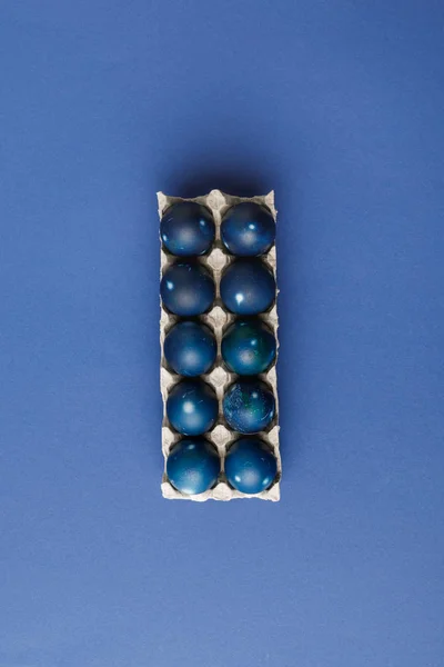 Vista superior de huevos de Pascua pintados de azul en bandeja de huevo sobre superficie azul - foto de stock