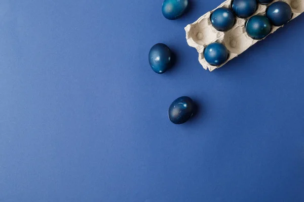 Vista superior de huevos de Pascua pintados de azul y bandeja de huevo en la superficie azul - foto de stock