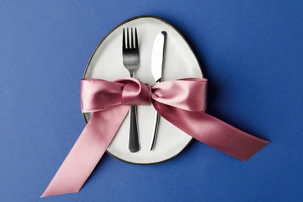 Top view of plate in shape of egg with fork and knife isolated on blue, easter concept — Stock Photo