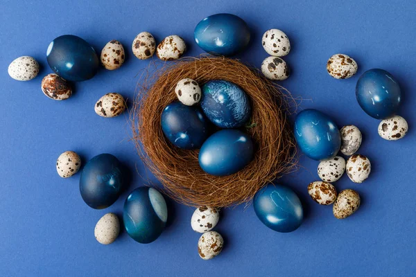 Blick von oben auf blau bemalte Ostereier und Wachteleier in dekorativem Nest auf blauer Oberfläche — Stock Photo