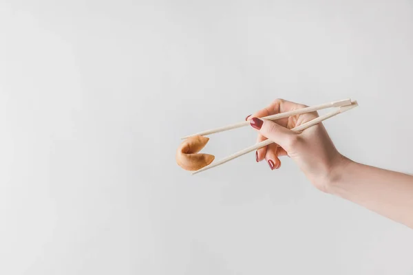 Imagen recortada de mujer sosteniendo galleta de la fortuna china con palillos aislados en blanco - foto de stock