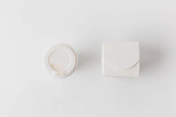 Vista dall'alto della tazza di caffè usa e getta e scatola di tagliatelle sulla superficie bianca — Foto stock