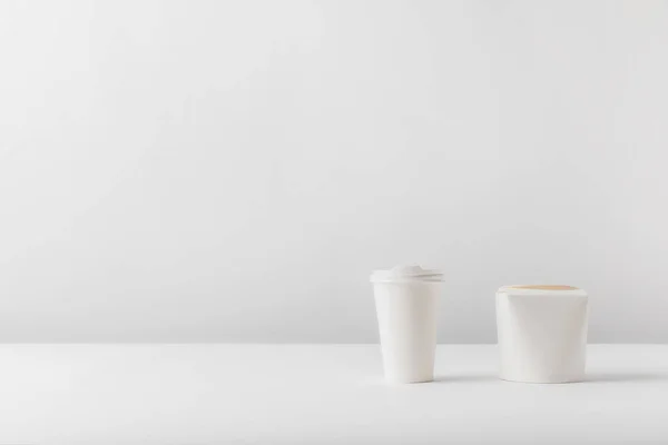 Taza de café desechable y caja de fideos en la superficie blanca - foto de stock