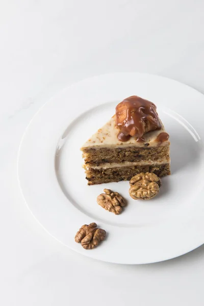 Cake on white plate surrounding by walnuts on table — Stock Photo