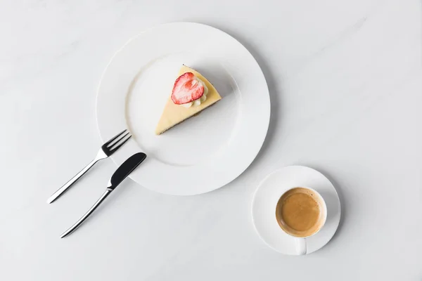 Tarta de queso con fresa en la parte superior y taza de café en la mesa - foto de stock