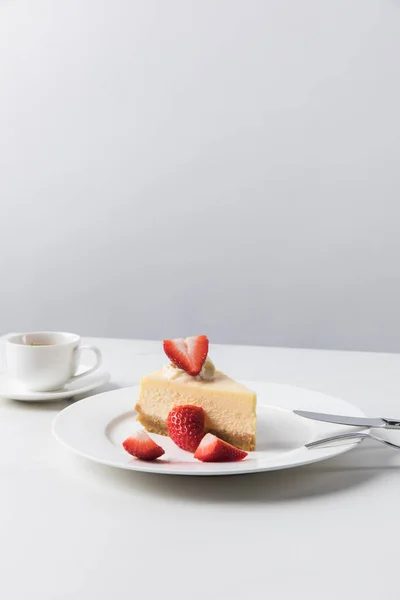 Cheesecake with strawberries on plate and cup of coffee on white table — Stock Photo