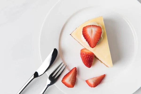 Placa con tarta de queso rodeada de fresas en rodajas - foto de stock