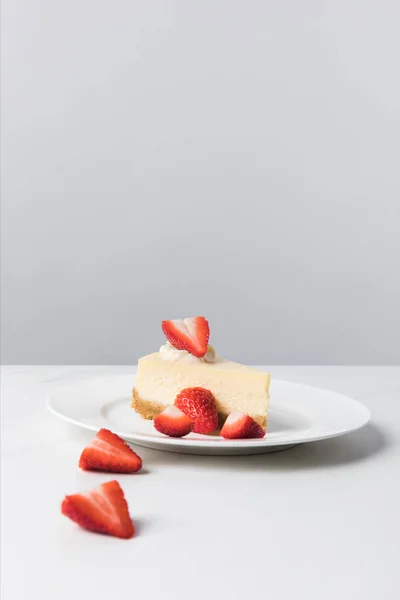 Closeup view of plate with cheesecake surrounding by sliced strawberries on table — Stock Photo