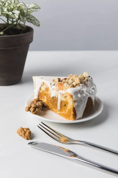 Kuchen auf Teller in der Nähe von Topfpflanze mit Gabel und Messer — Stockfoto