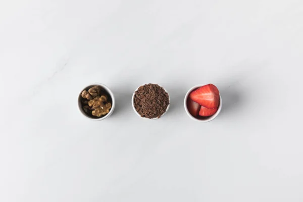 Tres cuencos con nueces, chocolate rallado y fresas en blanco - foto de stock