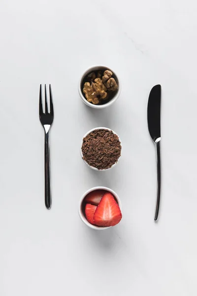 Tigelas com nozes, chocolate ralado e morangos entre garfo e faca, mesa concepção compromissos — Fotografia de Stock