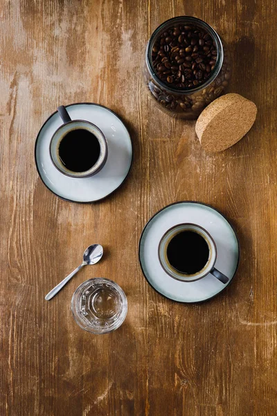 Two cups of black coffee and coffee beans in jar on wooden table — Stock Photo